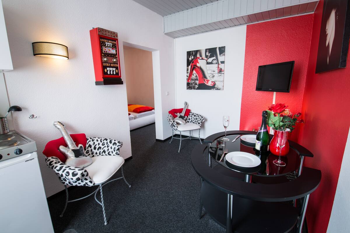 A modern room with a kitchenette, a dining area with a black table, and a red accent wall.