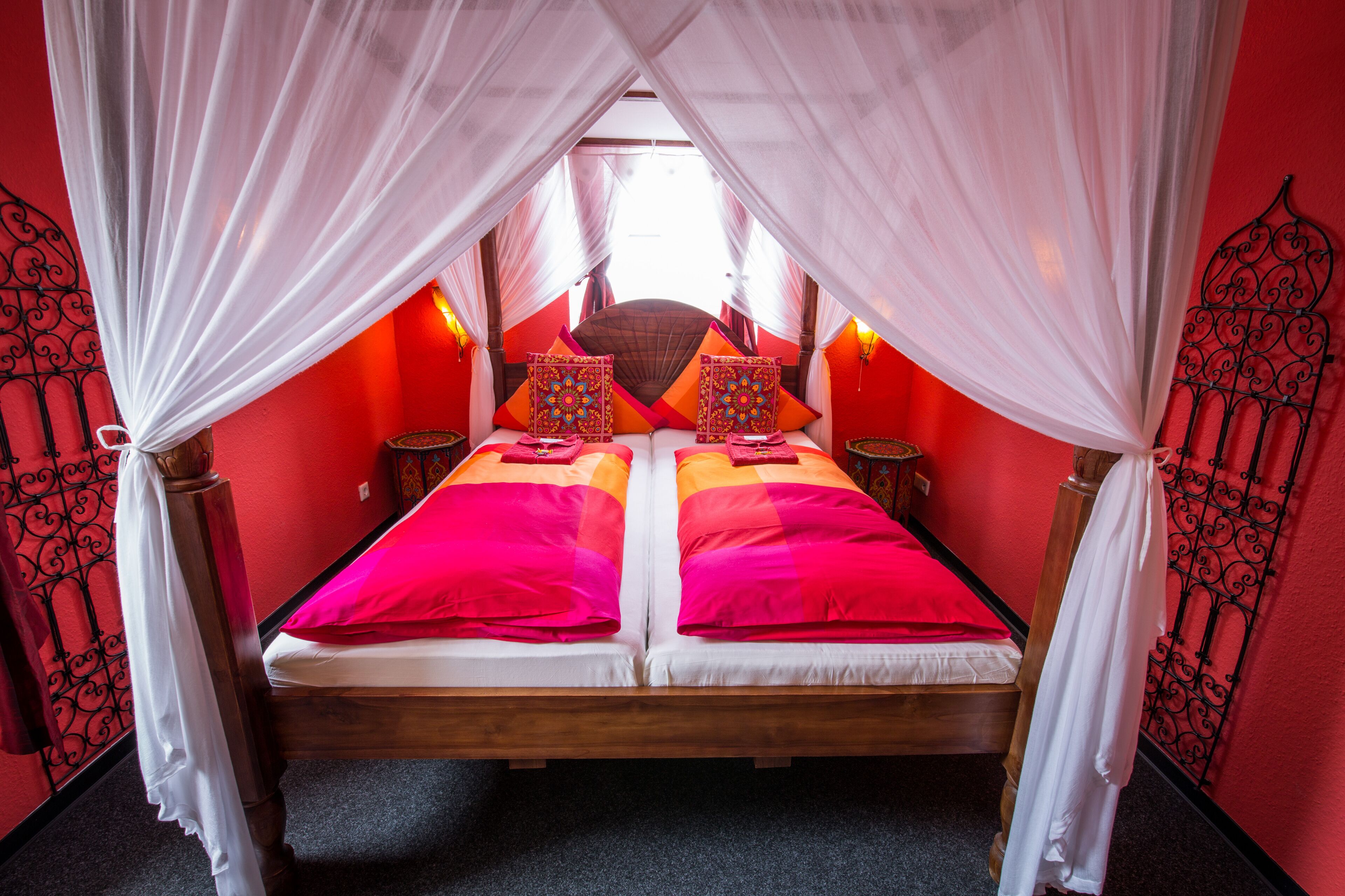 A bed with two pillows, a canopy, and a red wall.