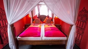 A bed with two pillows, a canopy, and a red wall.