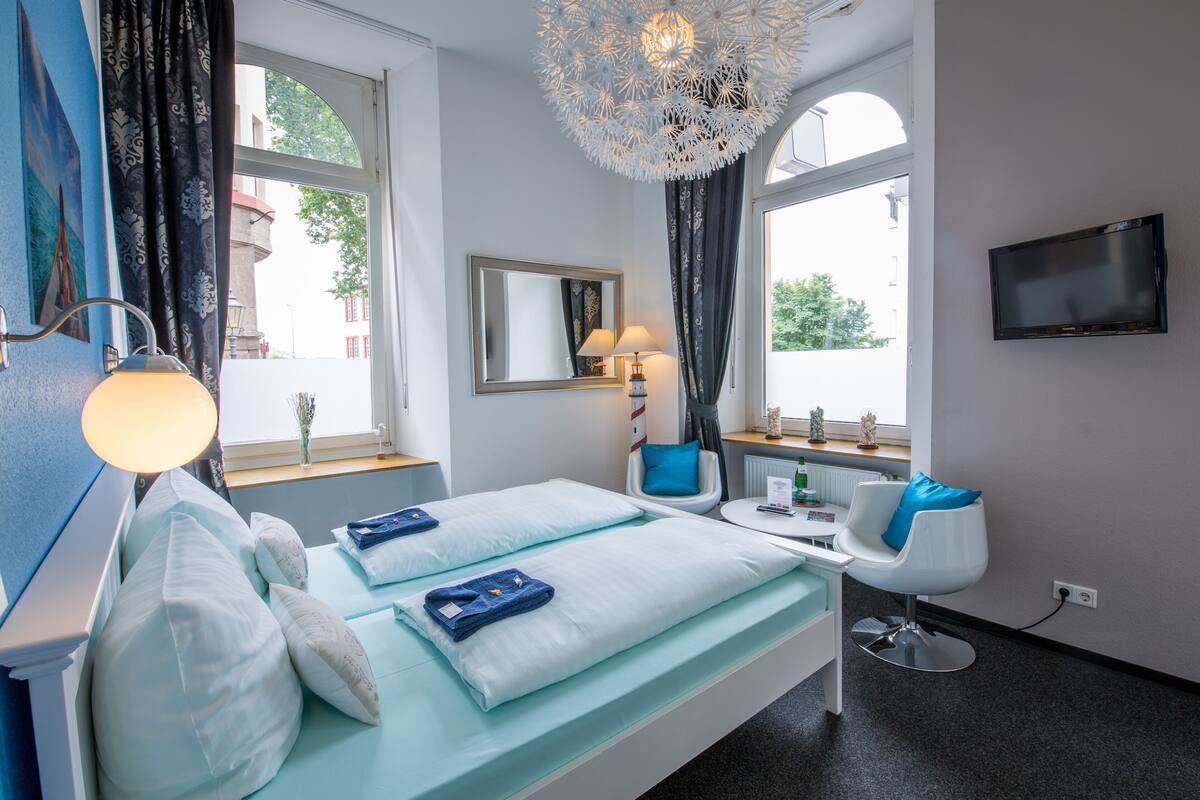 A hotel room with a bed, bedside table, lamp, chair, TV, and large windows.