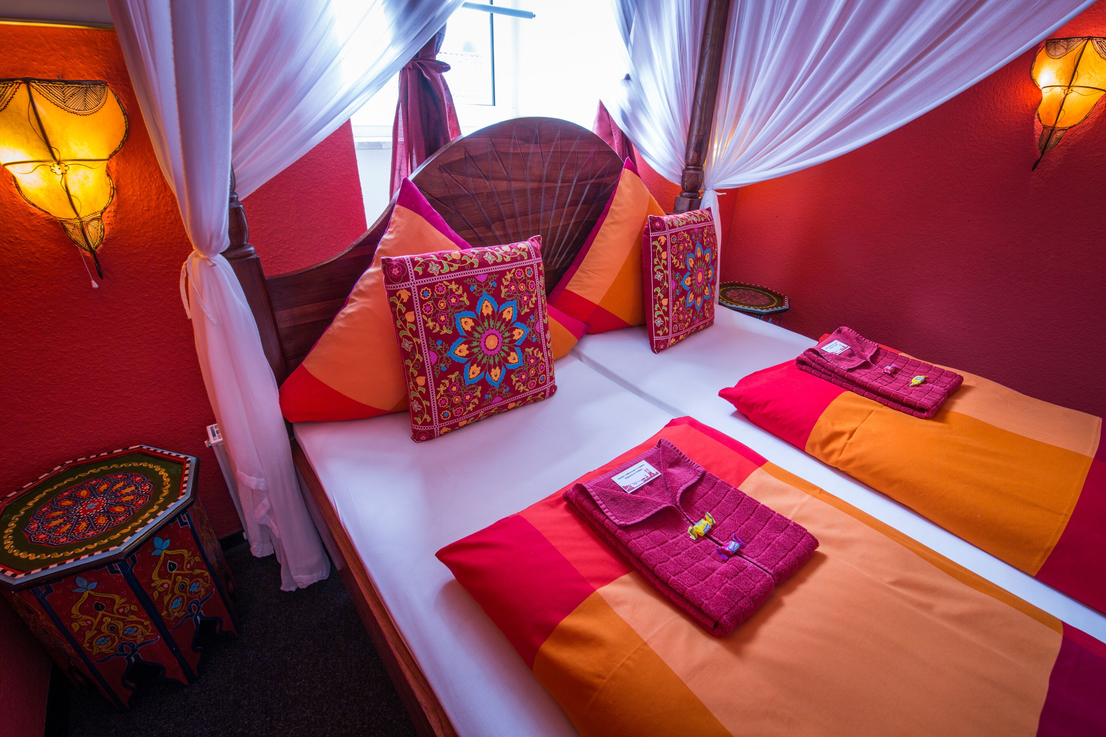 A room with a bed, a fan, and a table with a lamp.