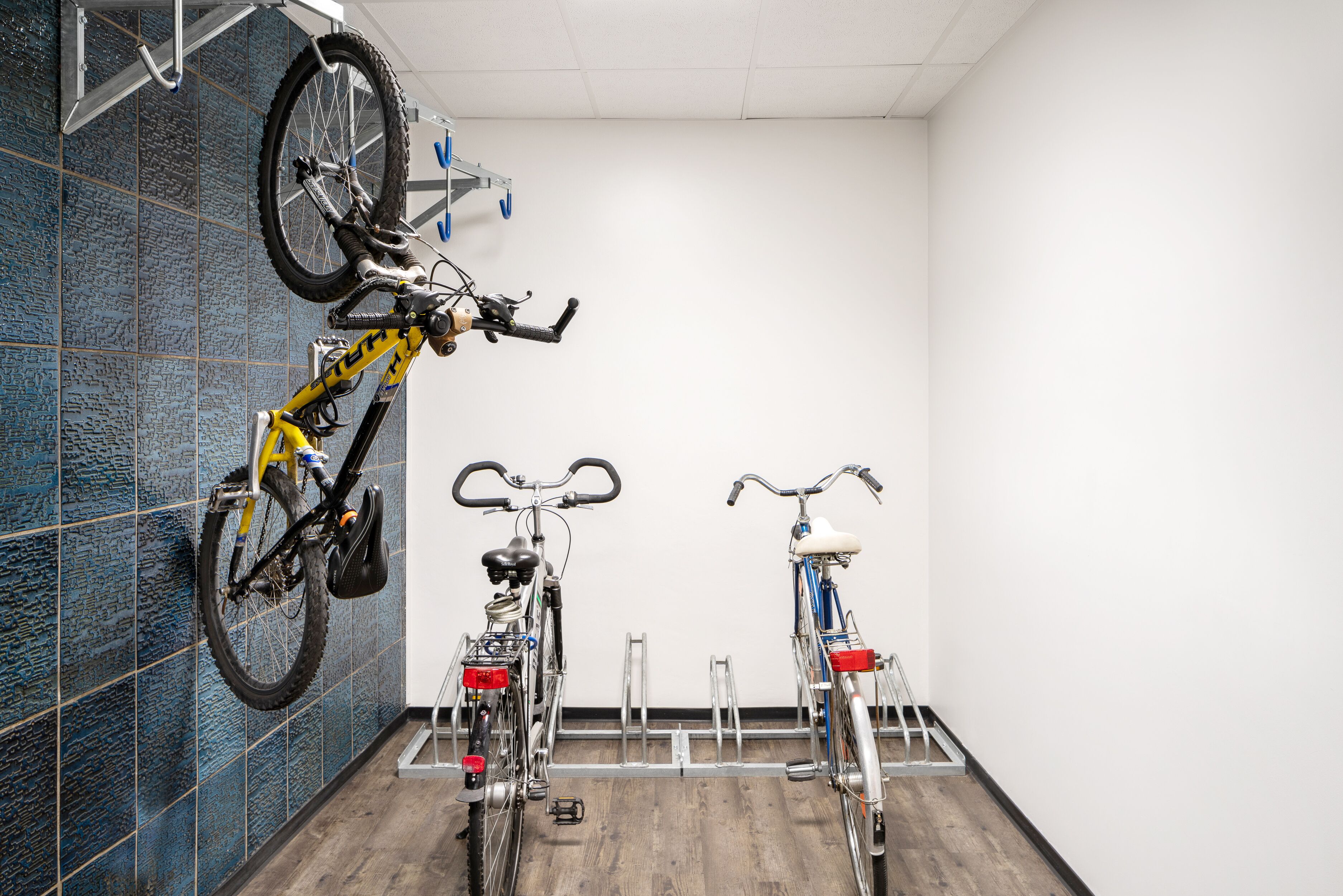 A room with two bicycles mounted on wall racks, a wooden floor, and a tiled wall.