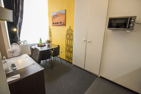 A compact hotel room with a dining area, a microwave, a radiator, and a painting of a desert scene. - Aparthotel am Münzplatz (Koblenz)
