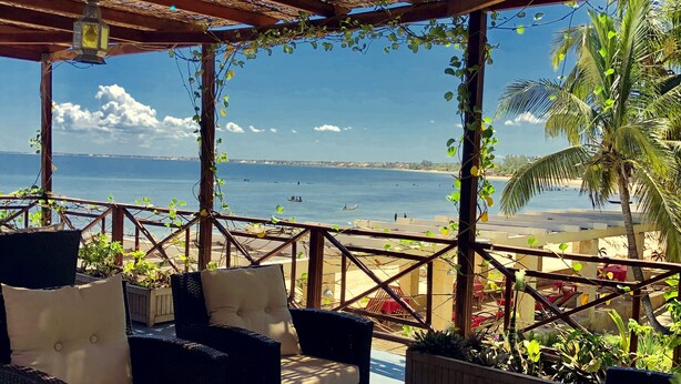 An outdoor seating area with wicker furniture and cushions, overlooking a beach and the sea. - Ifaty Beach Club (Ifaty)
