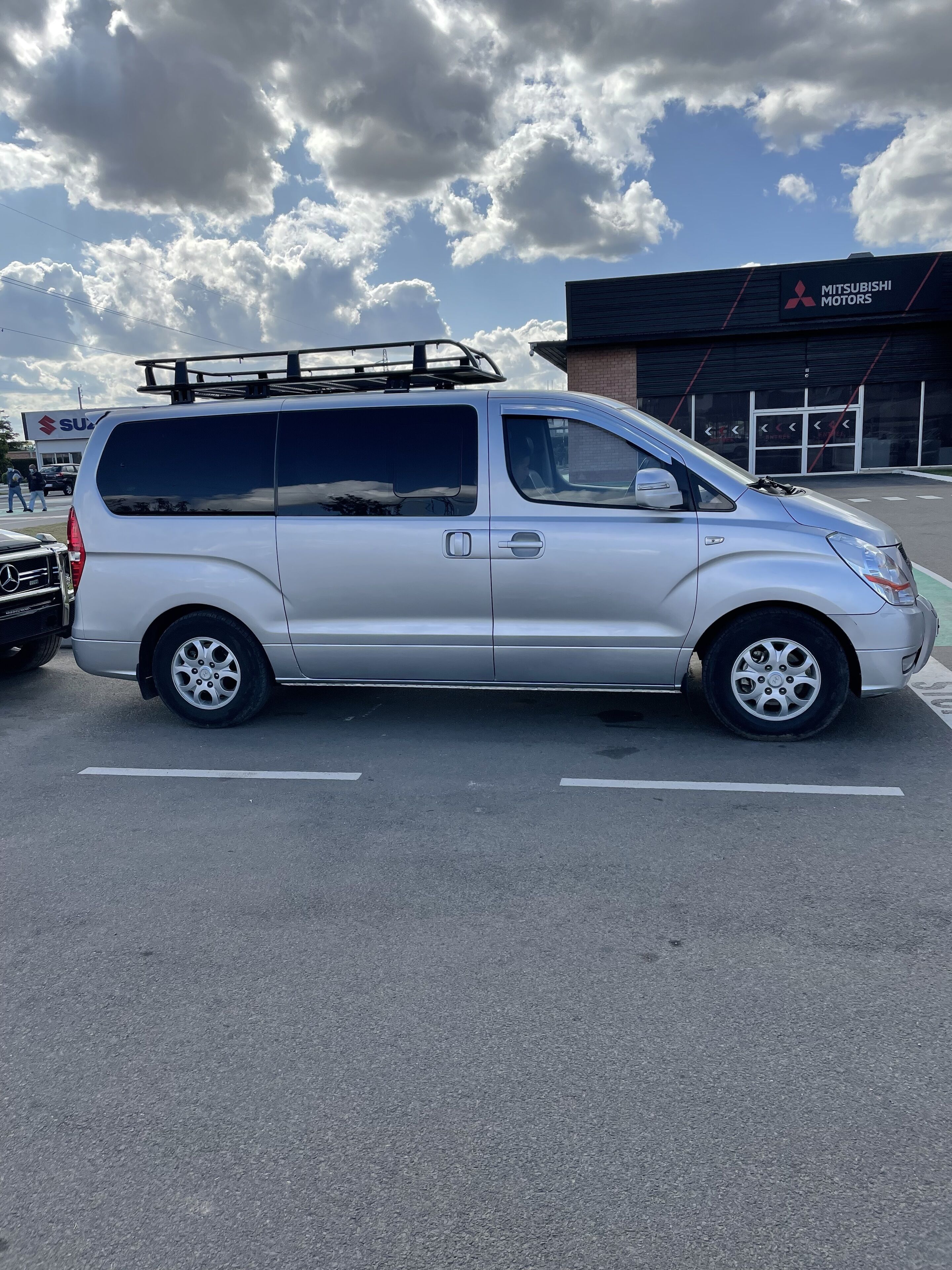 A silver van parked in a lot with a Mitsubishi Motors building in the background.