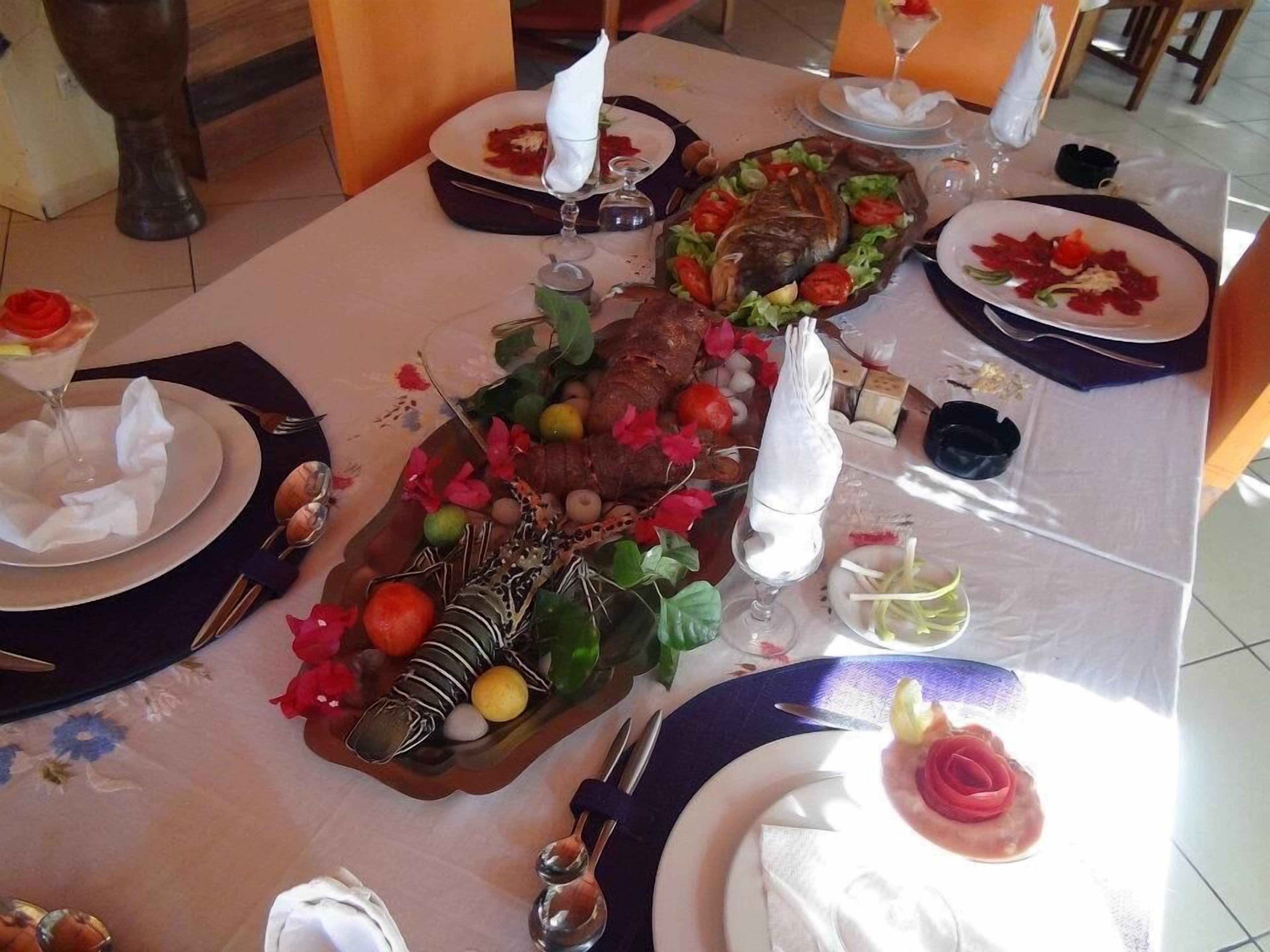 Une table à manger dressée avec des assiettes, des couverts et un centre de table décoratif comprenant un poisson rôti, des fruits et des fleurs.