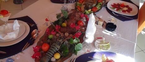 Une table à manger dressée avec des assiettes, des couverts et un centre de table décoratif comprenant un poisson rôti, des fruits et des fleurs.