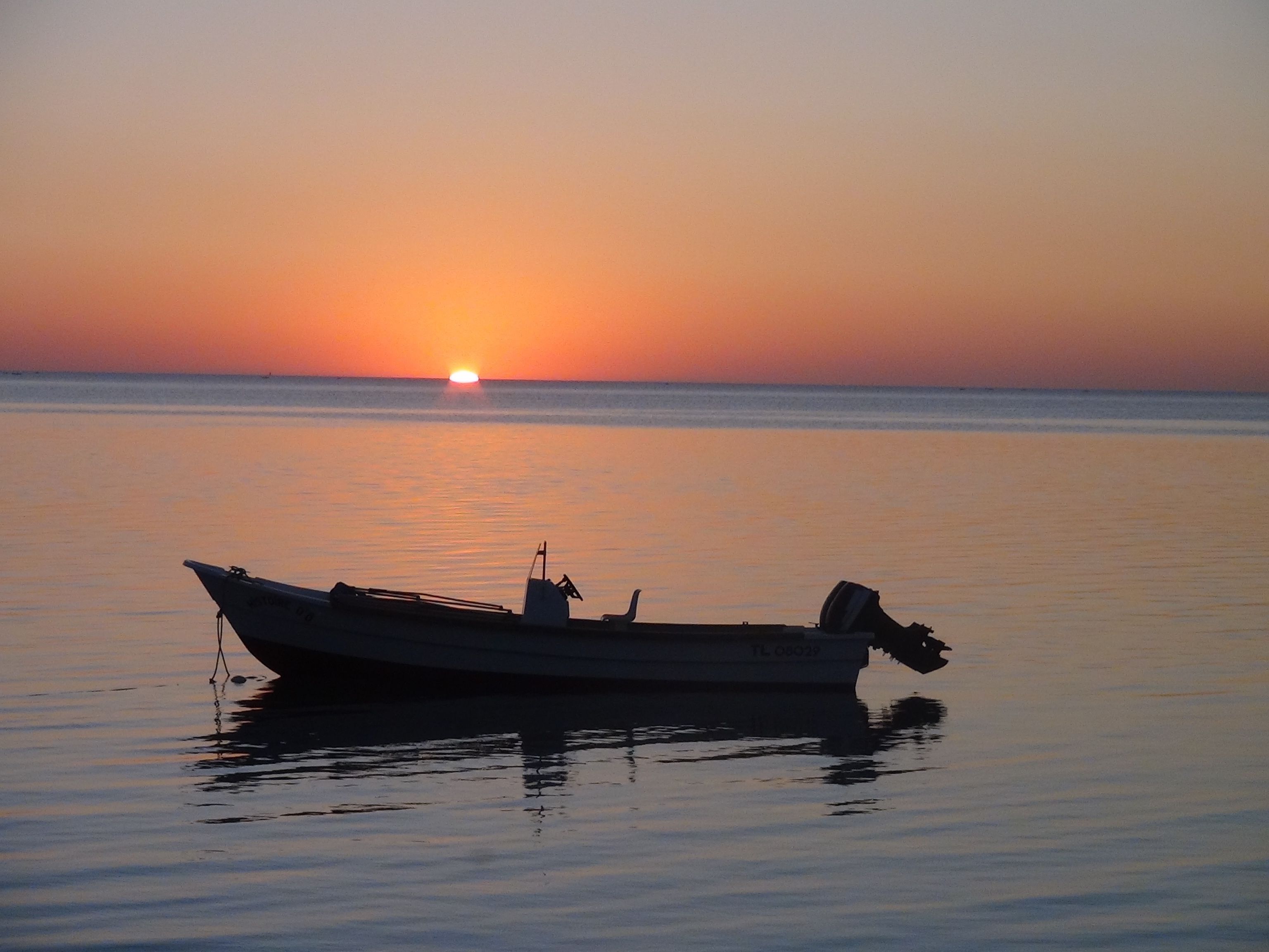A boat anchored on calm water during sunset.