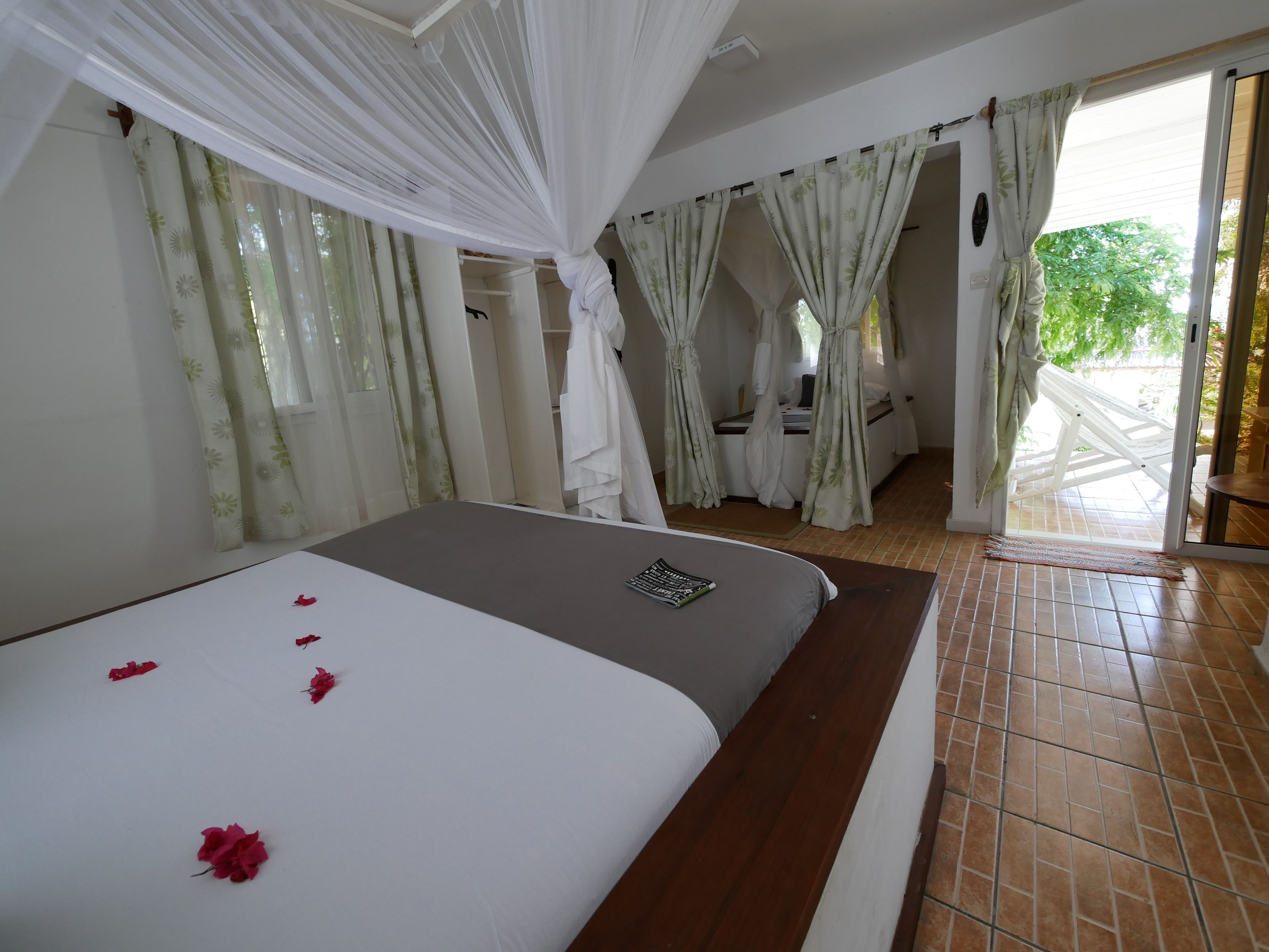 A bedroom with a bed, a bedside table, a window with curtains, and a view of the outside.