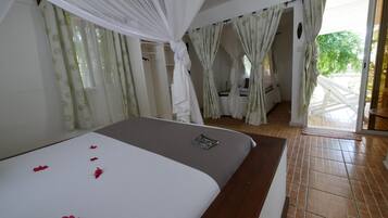 A bedroom with a bed, a bedside table, a window with curtains, and a view of the outside.