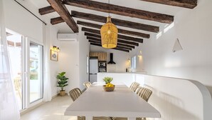 Zona pranzo con tavolo bianco, sedie, lampadario e cucina sullo sfondo.