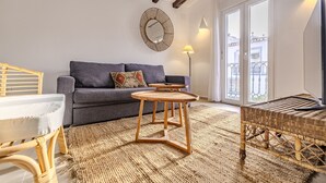 Un soggiorno con un divano, un tavolino in legno, una poltrona in vimini, una lampada da terra e un grande specchio appeso al muro.