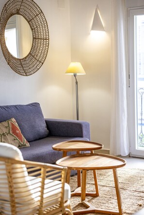 A living room with a sofa, two wooden side tables, a floor lamp, a woven mirror, and a wicker chair.