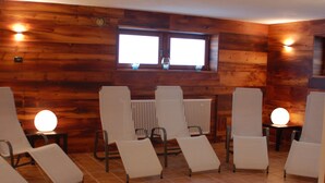 Quarto com paredes de madeira, uma janela e seis cadeiras brancas dispostas em duas fileiras.