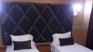 Dos camas individuales con cabeceras negras y ropa de cama blanca en una habitación con suelo de baldosas.