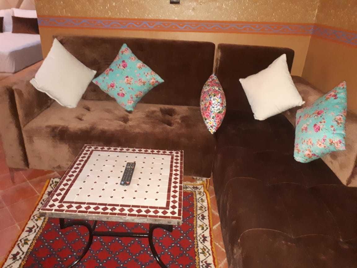 Un sofá marrón con cojines estampados, una mesita con diseño y una alfombra con motivos azules y rojos.