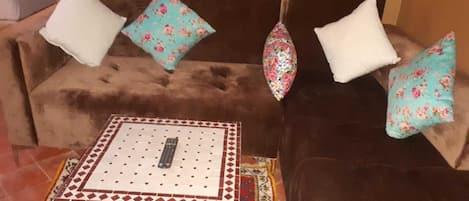 Un sofá marrón con cojines estampados, una mesita con diseño y una alfombra con motivos azules y rojos.