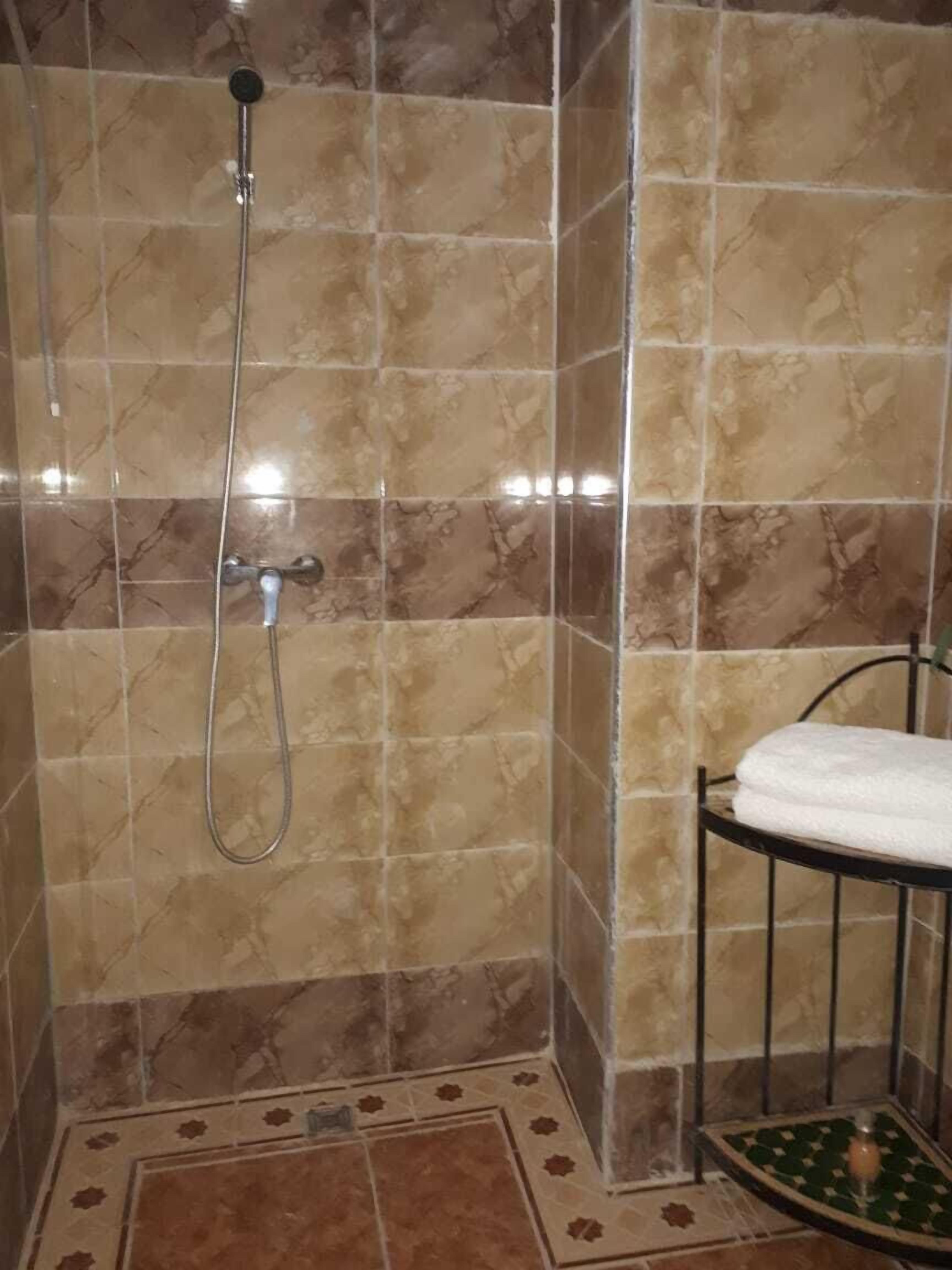 A shower with a handheld showerhead and a towel rack with a folded towel.