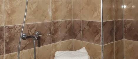 A shower area with a handheld showerhead and a wall-mounted faucet.