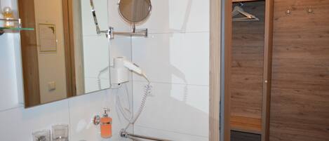Ein modernes Badezimmer mit einem weißen Waschbecken, einem Spiegel, einem Fön und einer Duschkabine aus Holz.