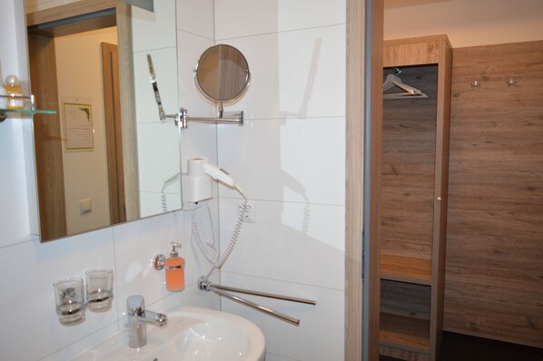 Un baño moderno con un lavabo blanco, un espejo, un secador de pelo y un box de ducha de madera.