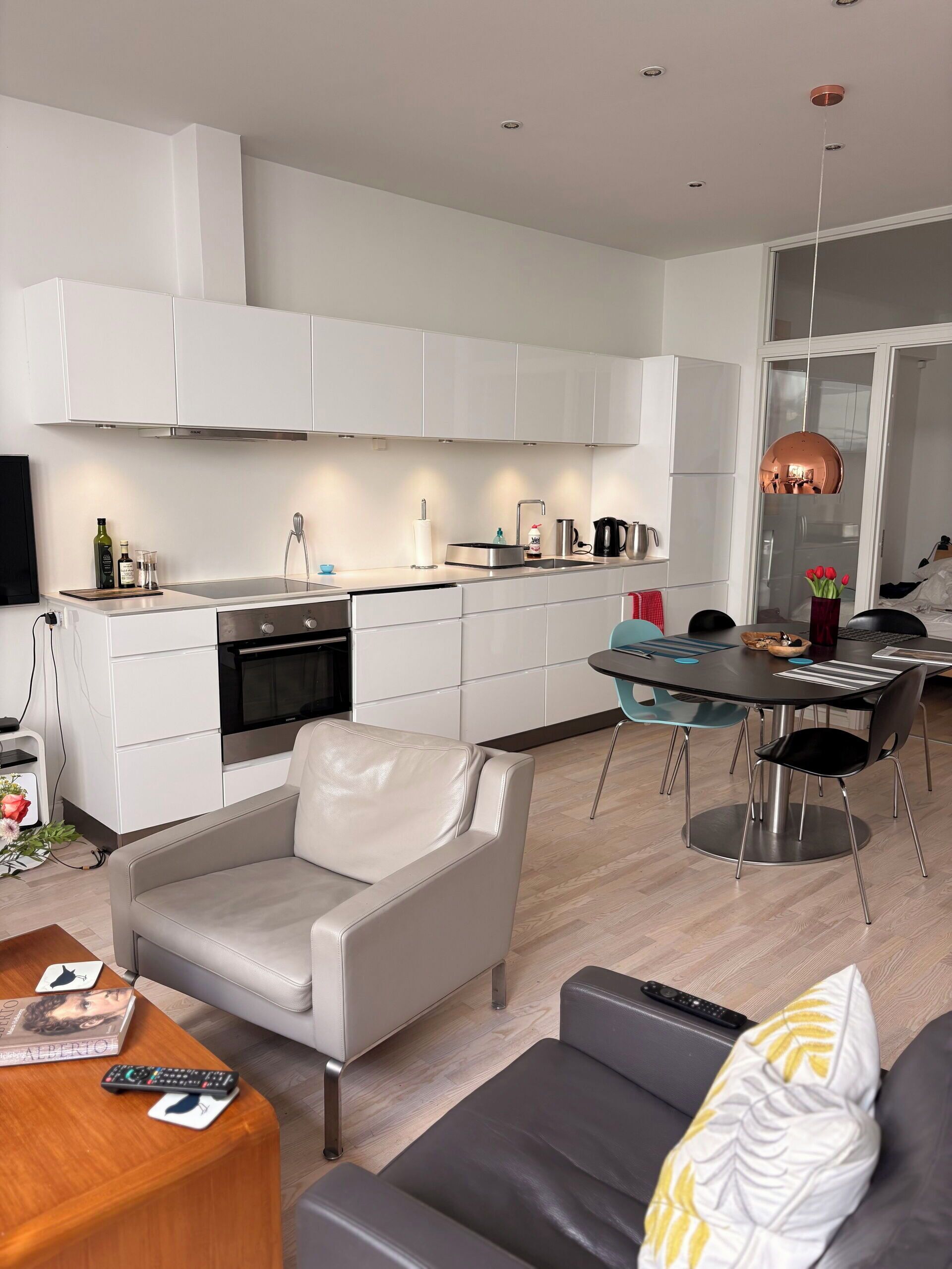 A modern kitchen with white cabinets, a built-in oven, and a dining area with a table and chairs.