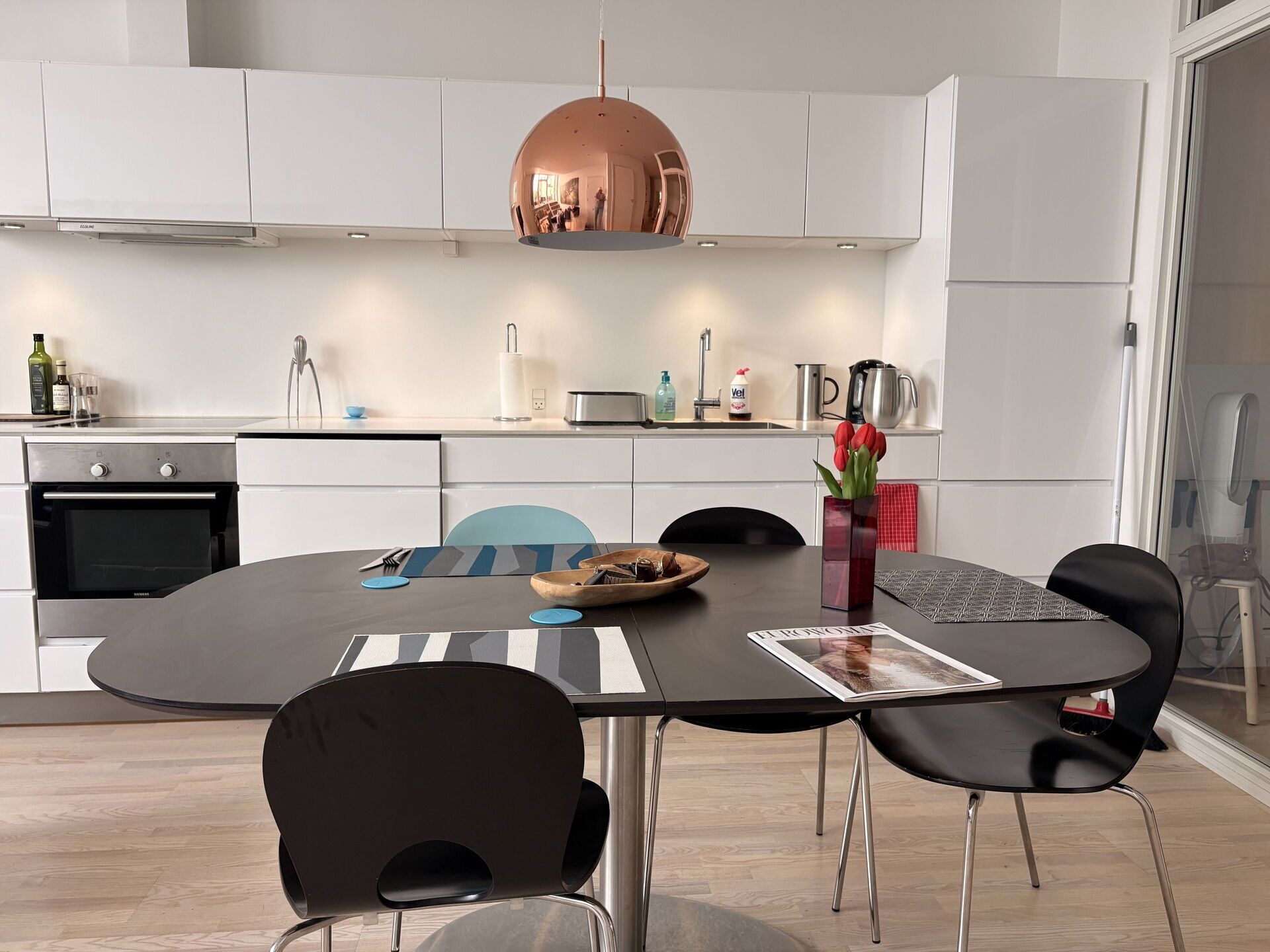A modern kitchen with white cabinets, a stainless steel range, and a dining area with a round table and black chairs.