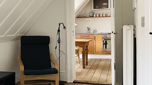 Een kamer met een houten stoel, een keuken op de achtergrond en een deur naar een andere kamer.
