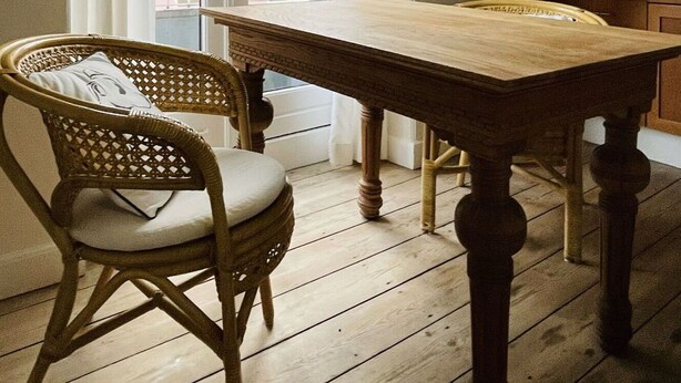 Een kamer met een houten tafel, een rieten stoel en een hanglamp.