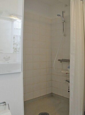 A small, white-tiled bathroom with a shower, a toilet, and a sink.