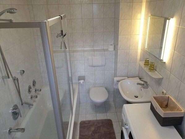 Un baño moderno con ducha de mampara de vidrio, inodoro, lavabo y espejo.