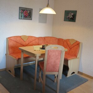 A room with a wooden table, a single orange chair, and a bench with a light fixture above. - Hiking, mountains and lake (Gottmadingen)