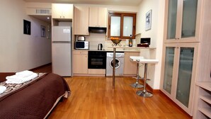 Une chambre d’hôtel compacte comprenant un coin cuisine, un lit recouvert d’une housse marron, un lave-linge et un petit coin bar.