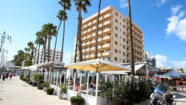 Un hôtel situé en bord de mer, doté d’une terrasse et bordé de palmiers.