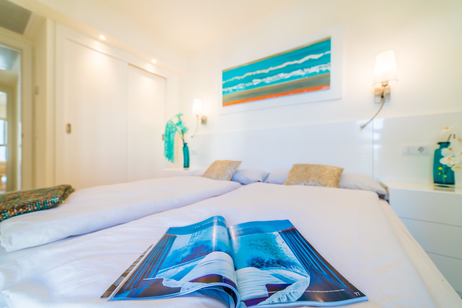 Ein Hotelzimmer mit zwei Betten, einem großen Gemälde an der Wand und einer Zeitschrift auf dem Bett.