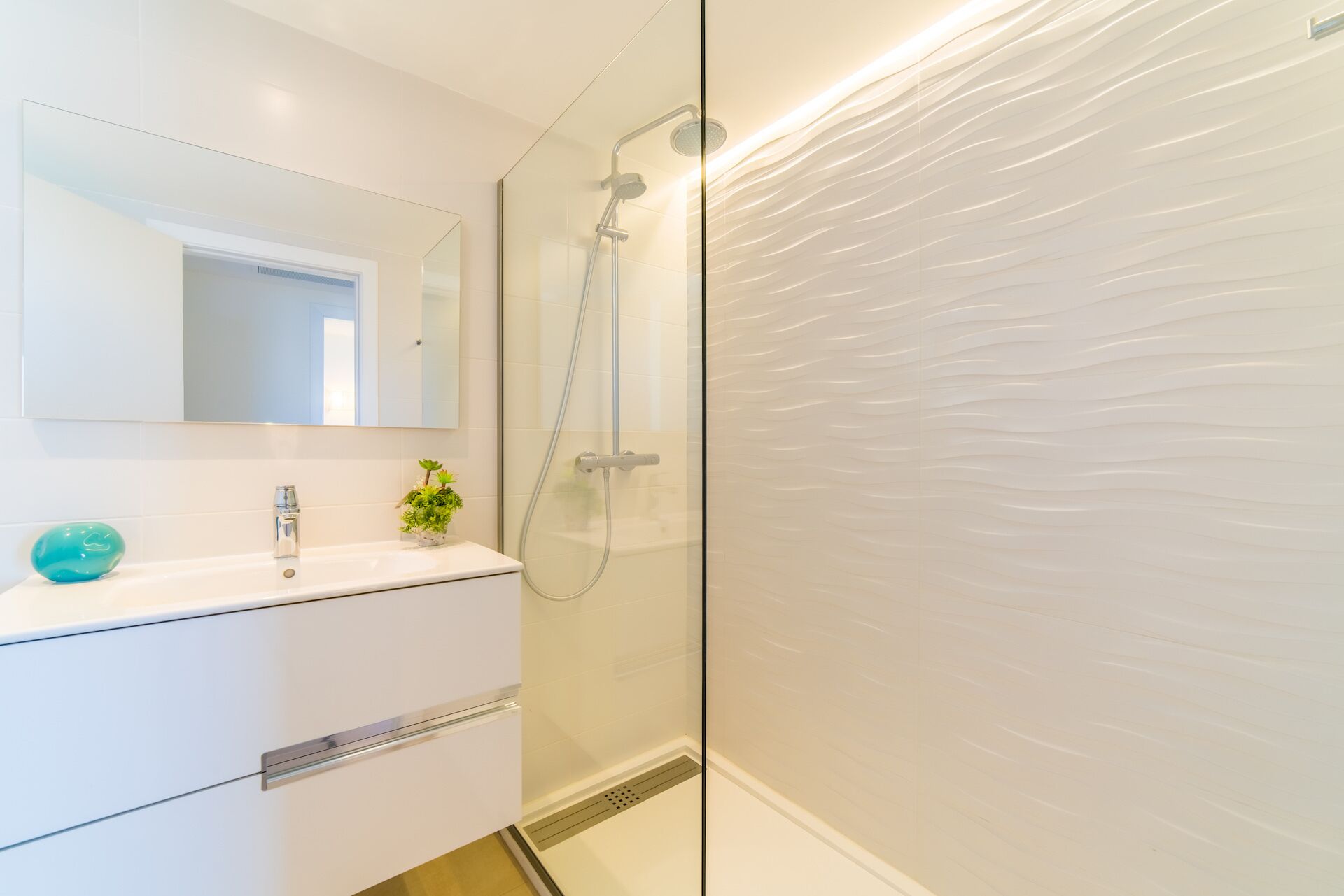 Une salle de bain moderne avec une douche à parois de verre, un meuble-lavabo blanc avec un miroir et une petite plante en pot.
