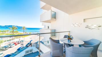 Ein Balkon mit Korbstühlen und einem Tisch, der Blick auf einen Strand und einen Parkplatz bietet.