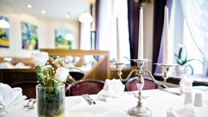 A dining table set with a candle holder, a glass vase with flowers, and a folded napkin. - Parkhotel Meerane (Meerane)