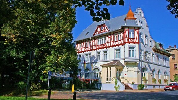 A historic building with a distinctive red and white facade, large windows, and a prominent corner tower. - Parkhotel Meerane (Meerane)