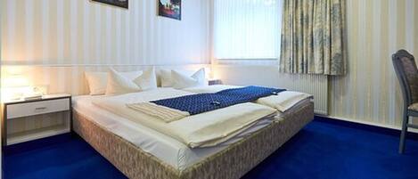 Una habitación de hotel con una cama grande, una mesita de noche, una silla y una ventana con cortinas.