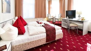 A hotel room with a large bed, a desk with a chair, a television, and a dining table with chairs. - Parkhotel Meerane (Meerane)