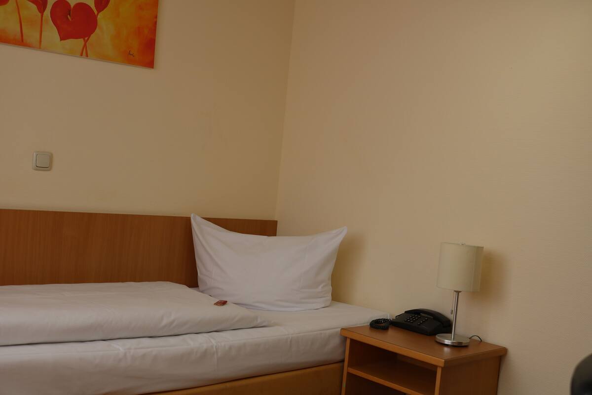 A hotel room with a bed, a bedside table with a lamp, and a telephone.