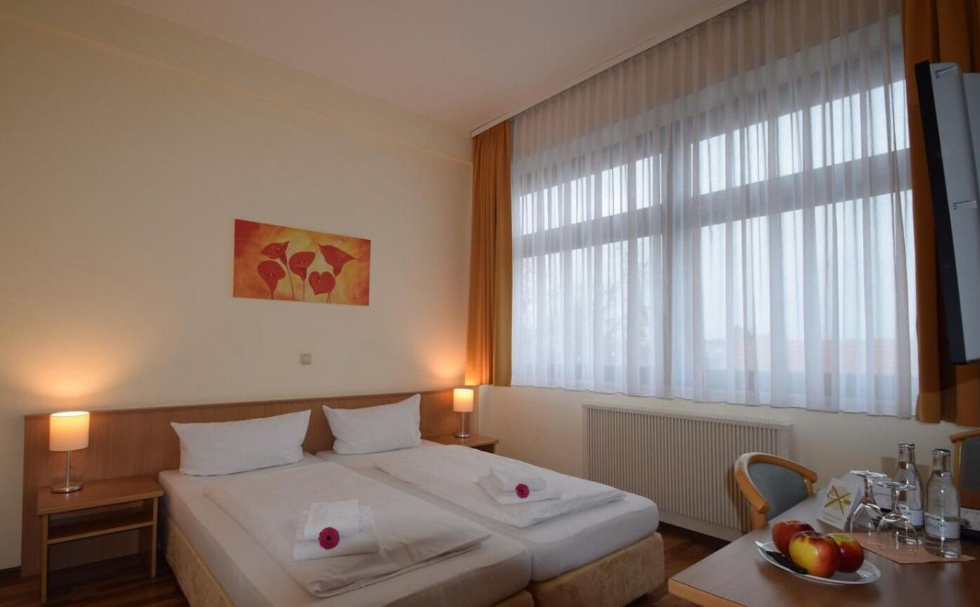 A hotel room with two beds, a dining table with fruit, and a painting on the wall.