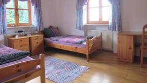 Un dormitorio con dos camas de madera, un tocador de madera, un escritorio y una ventana con cortinas.