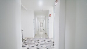Un pasillo largo y estrecho con piso de diseño geométrico, paredes blancas y puertas a ambos lados.