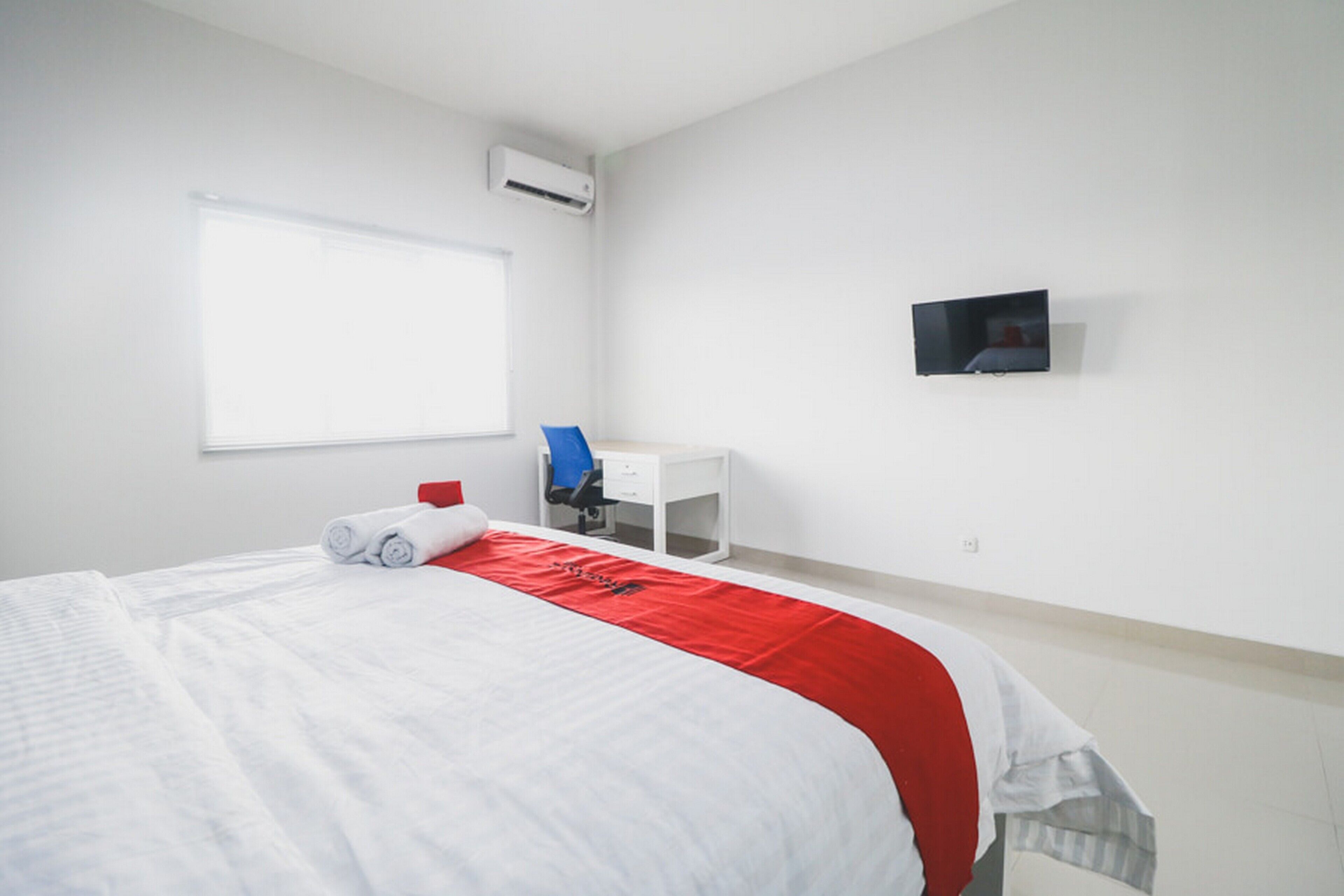 Habitación de hotel con cama, escritorio, silla, televisor y aire acondicionado.