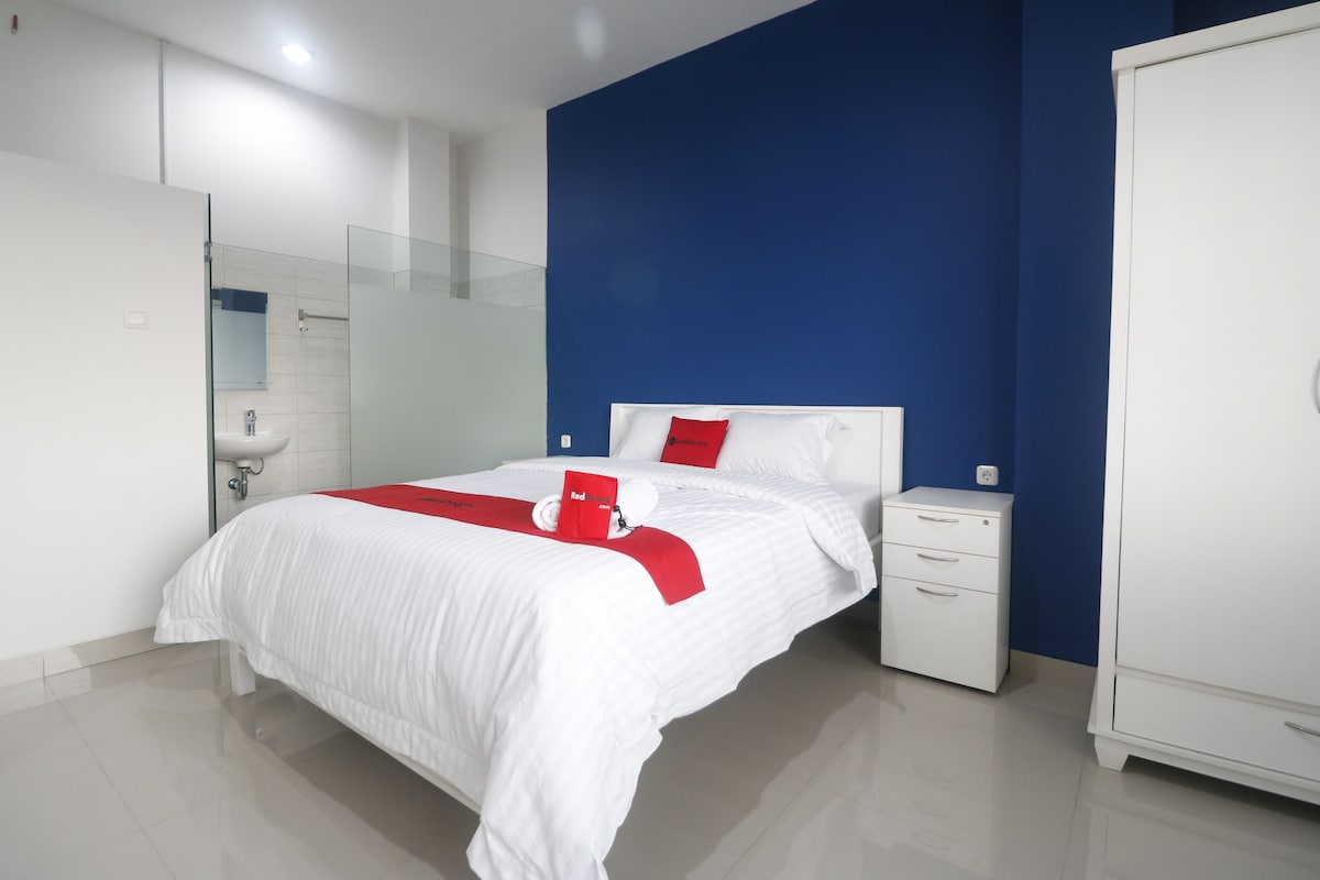 A hotel room with a bed, a nightstand, a wardrobe, and a bathroom with a glass shower enclosure.