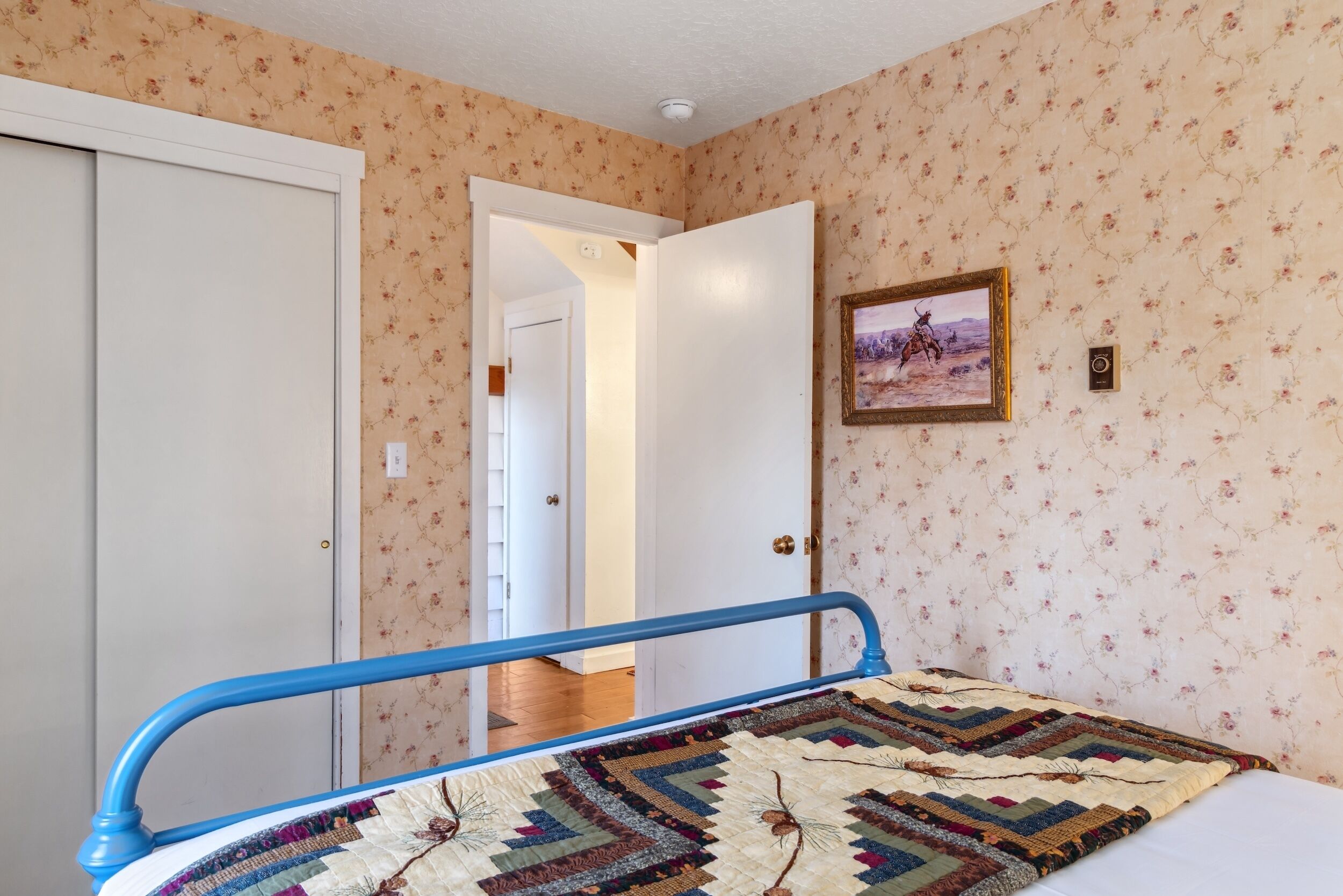 Een slaapkamer met een bed, een sprei, een deur en een wand met bloemenbehang.