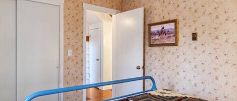 A bedroom with a bed, a quilt, a door, and a wall with floral wallpaper.