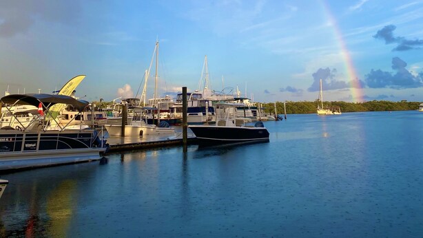 A marina with boats docked, a rainbow in the sky, and calm water. - Houseboat offers a rooftop deck for stunning views of the sunrise and sunset. (Tavernier)